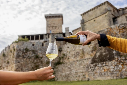 Dos personas brindando con vino frente a una construcción de piedra.